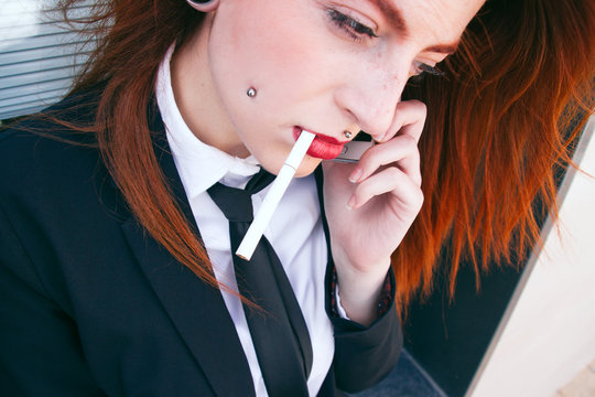 Ejecutiva pelirroja vestida de traje fumando un cigarrillo 