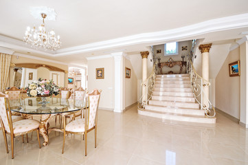 A luxurious interior with a dining area and marble floor and stairs with forged rails.