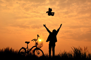 Silhouette of girl with bicycle on grass field at the sky sunset, color of vintage tone and soft focus concept journey