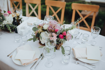 Festive stands in the wedding banquet area served with dishes and cutlery and decorated with compositions of flowers, greenery and candles