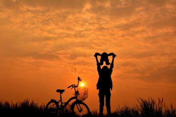 Silhouette of girl with bicycle on grass field at the sky sunset, color of vintage tone and soft focus concept journey