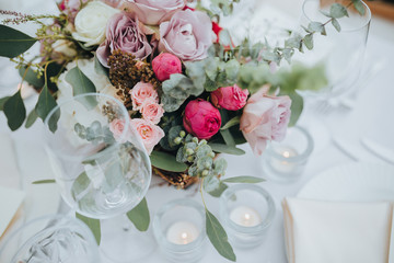 Festive stands in the wedding banquet area served with dishes and cutlery and decorated with compositions of flowers, greenery and candles