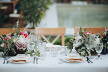 Festive stands in the wedding banquet area served with dishes and cutlery and decorated with compositions of flowers, greenery and candles