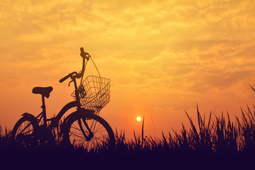 Naklejka premium Silhouette of bicycle on grass with the sky sunset