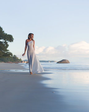 Beautiful, sexy blonde woman walks at tropical beach, long dress