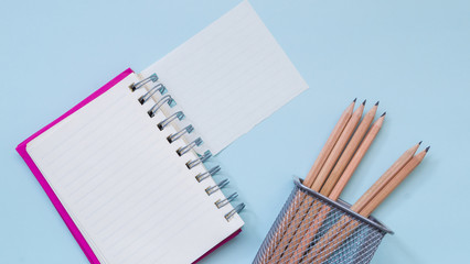 Torn notebook and pencils in basket on blue background view from above