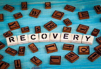 recovery word written on wood block. Wooden alphabet on a blue background.