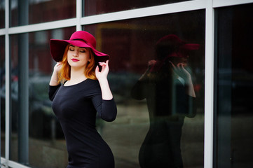Portrait of fashion red haired girl on red hat and black dress with bright make up posed against...