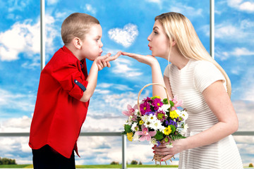 Obraz premium Young beautiful mother and son blow kisses .A woman and a boy with a bouquet,a basket of flowers. Spring concept of family vacation and family love. Women's day 