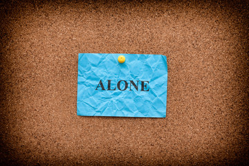 Blue crumpled paper with word Alone on a cork board