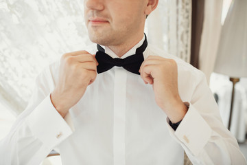 Man fixes black bow tie on his neck