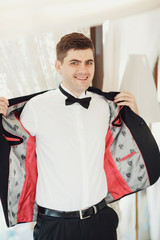 Smiling man puts on black jacket standing in bright room