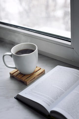 Fototapeta na wymiar Cozy home still life: cup of hot coffee or tea and opened book on windowsill. Education concept, free copy space