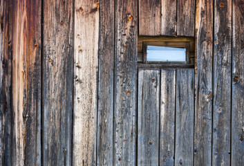 Wall of old weathered wooden planks with small window on it.