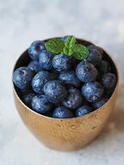 Ripe wet blueberries and a sprig of mint  in a golden glass on a gray background