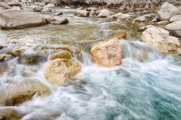 A river of fresh water among the rocks. Fresh aqua fast flow in the stones. A forest river with clean cold water. Fresh spring in the mountains. Concept of drinking water