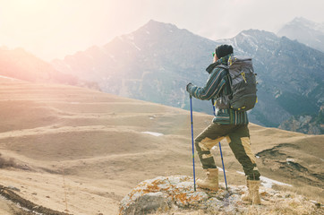 A guy with a beard and wearing sunglasses in a membrane jacket, hat, with a backpack and sticks for...