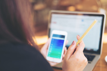 A woman's hand holding and using a smart phone with laptop on the table in office