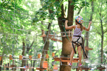 Fototapeta na wymiar adventure climbing high wire park - girl on course in mountain helmet and safety equipment