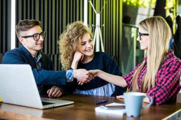 Young students are using gadgets, talking and smiling while working at the modern office. Men and woman are handshaking