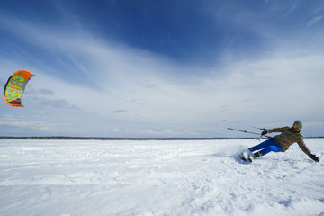 Sportsman in bright clothes is riding with kite on winter snow-covered frozen sea