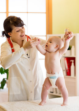 Happy cute baby at health exam at doctor's office. Pediatrician supports infant kid while he is standing