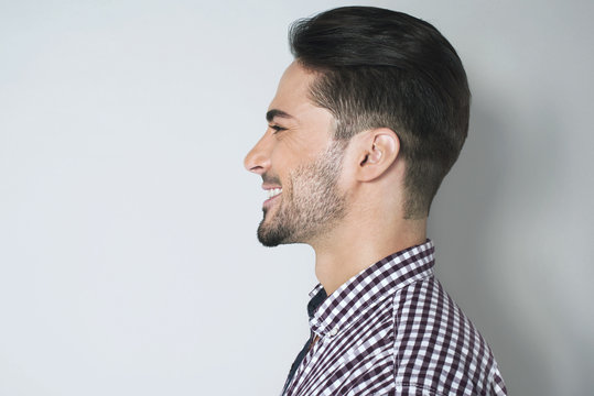 Handsome profile portrait of young man. Lovely appearance side look of smiled dark haired man in plaid shirt against light gray background