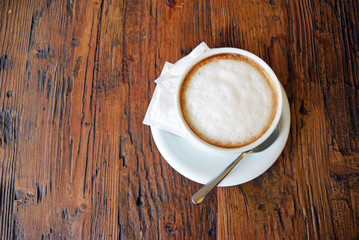 top view on cup of cappuccino with spoon on the wooden table background