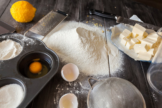 Ingredients for the dough. Eggs, flour, butter, sugar, lemon and kitchen tools on a dark wooden background. Rustic background. The process of making cakes for a cake Napoleon