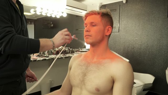 Makeup master sprays orange color to the model's face from aerograph