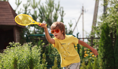 Cute boy wearing orange sunglasses plays beach tennis in the garden © Tatiana Murr