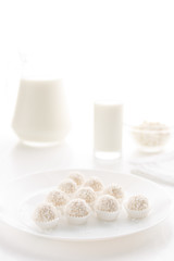 Raffaello candy in baskets on a plate, with milk in a glass and jug, cottage cheese in a bowl in the background, on a white table, in a high key, with space for text