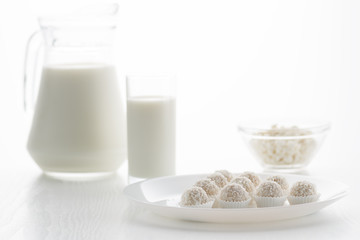 Raffaello candy in baskets on a plate, with milk in a glass and jug, cottage cheese in a bowl in the background, on a white table, in a high key, with space for text
