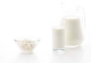 Milk in a glass and jug, cottage cheese in a bowl, on a white table, in a high key, with space for text
