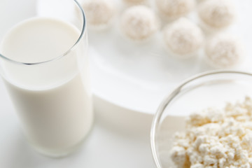 Milk in a glass, candy Raffaello cottage cheese in a bowl in the background, on a white table, in a high key