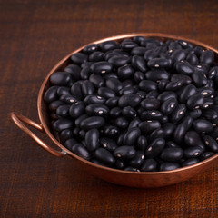 Black beans in scoop on wooden background