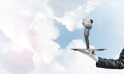 Businessman on metal tray playing fife against blue sky background