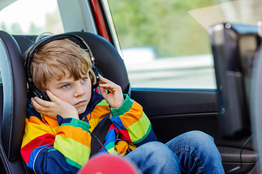 Little blond kid boy watching tv or dvd with headphones during long car drive