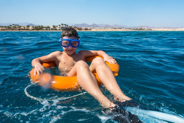 Smiling boy floating on lifebuoy in the sea