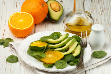 Organic avocado and spinach salad with orange and olive oil in a white plate on old wooden table.  vegetarian dish. Selective focus