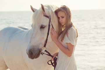 Girl in white dress with horse on the beach