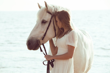 Girl in white dress with horse on the beach