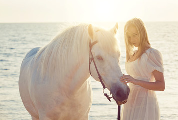 Girl in white dress with horse on the beach