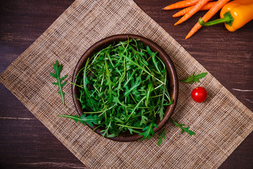 Arugula leaves in bowl. Fresh salad. Carrot, pepper and cherry tomato. Natural raw vegetables. Organic bio food on rustic wooden table.