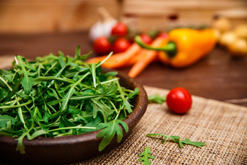 Arugula leaves in bowl. Fresh salad. Carrot, pepper and cherry tomatoes. Natural raw vegetables. Organic bio food on rustic wooden table.