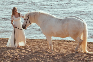 Girl in white dress with horse on the beach