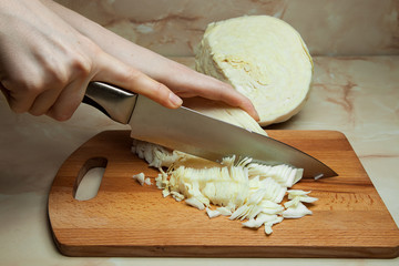 Woman's hand with a knife cutting the cabbage to prepare the lazy cabbage rolls or meatballs