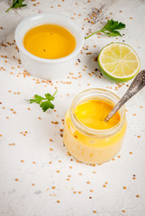 Ingredients for cooking healthy light dressings for vegetable salad: lemon (lime), olive oil, mustard, greens, on white concrete table, copy space vertical