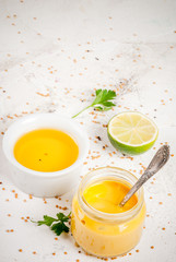 Ingredients for cooking healthy light dressings for vegetable salad: lemon (lime), olive oil, mustard, greens, on white concrete table, copy space vertical