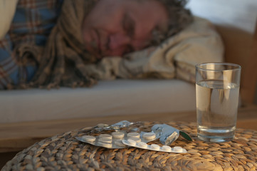 Ein Mann liegt mit Erkaeltung im Bett / Ein Mann liegt mit Erkaeltung im Bett, vor ihm liegen Medikamente, geringe Tiefenschaerfe.